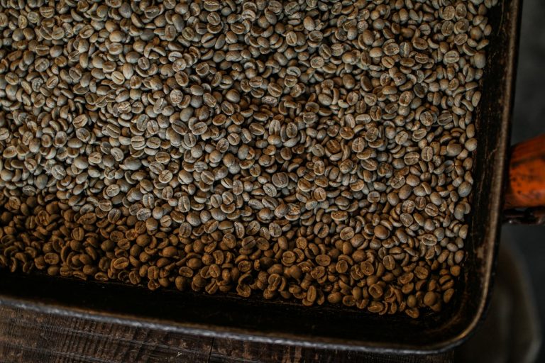 A large pile of unroasted coffee beans in a tray, perfect for coffee-related content.